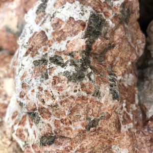 Puede incluir: Primer plano de una roca rugosa, marrón y blanca con vetas verde oscuro. La roca tiene un aspecto moteado.