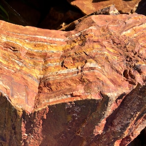 May include: A large, rough, red and brown rock with visible layers of white and gold minerals. The rock has a natural, unpolished surface.
