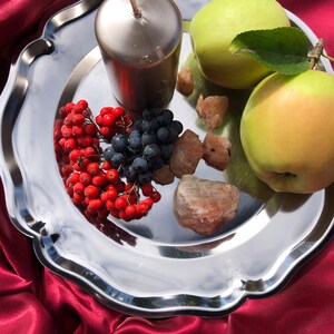 Peut inclure: Un plateau argenté avec une bougie argentée, deux pommes vertes, des baies rouges, des raisins bleus et des cristaux roses.