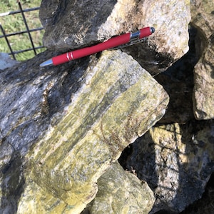 Peut inclure: Gros plan sur un tas de roches rugueuses grises et vertes avec un stylo rouge posé dessus.