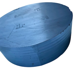 Könnte beinhalten: Ein dunkelgrauer, zylindrischer Silizium-Ingot mit einer glatten, flachen Oberseite, die schwache, lasergravierte alphanumerische Markierungen aufweist. Die Seite des massiven, metallisch wirkenden Objekts zeigt feine, horizontale Rillen.
