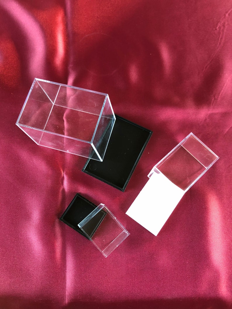 May include: Three clear acrylic display boxes with black bases. The boxes are different sizes and are arranged on a red satin fabric background.
