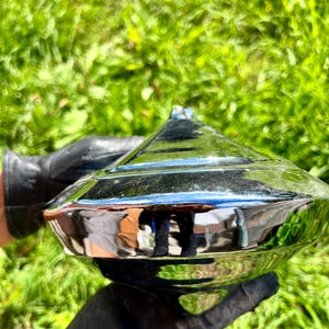 Könnte beinhalten: Ein poliertes Metallobjekt mit Chrom-Finish und einer facettierten, diamantartigen Form. Die Oberfläche ist stark reflektierend und zeigt verzerrte Umgebungsspiegelungen auf ihren zahlreichen winkligen Ebenen sowie eine Spitze.