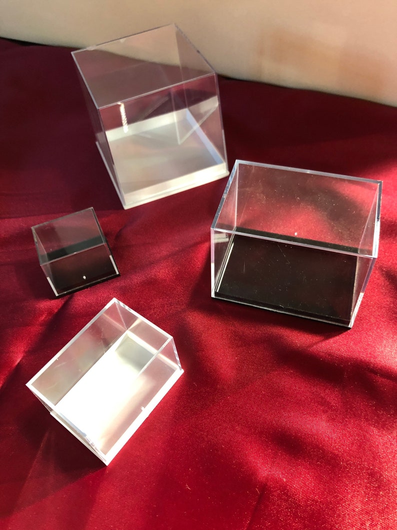 May include: Four clear acrylic display boxes of varying sizes. The boxes have white bases and black felt lining. The boxes are arranged on a red surface.