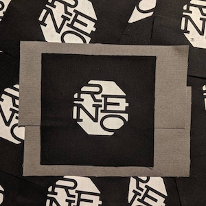Könnte beinhalten: Ein schwarzer Stoff-Patch mit einer weißen achteckigen Form, die das Wort "RE:NO" in einer stilisierten Schrift enthält.