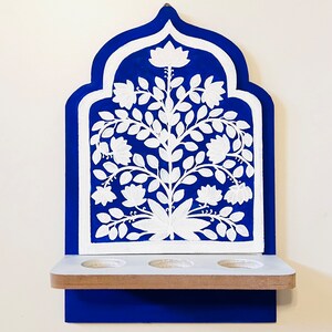 May include: A blue and white wooden wall shelf with an arched top. The shelf features a white floral design and three circular cutouts. The shelf is painted in a vibrant blue with white accents, creating a decorative piece.