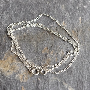 May include: A silver chain necklace with a lobster clasp fastening. The chain is made of small, oval-shaped links.