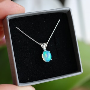 Könnte beinhalten: Eine silberne Kettenkette mit einem zarten ovalen Opal-Anhänger. Der Opal ist hellblau-grün mit Regenbogen-Schimmer.