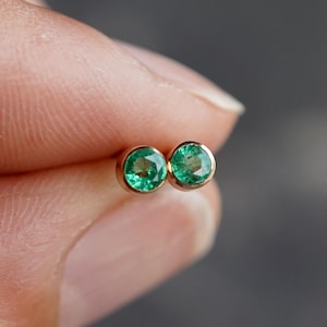 May include: A pair of emerald green gemstone earrings set in gold.