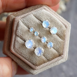 May include: A set of six silver moonstone earrings in a velvet jewellery box. The earrings are round and have an iridescent sheen.