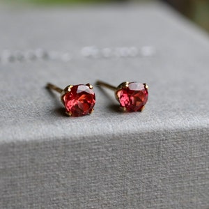 May include: A pair of gold stud earrings with small, round, red gemstones.