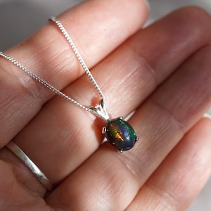 Peut inclure: Un collier en argent avec un pendentif en opale ovale foncé. L'opale présente des reflets irisés verts, bleus et rouges.