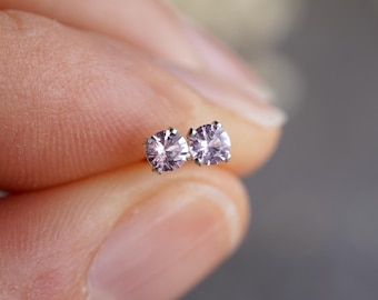 May include: A pair of small, round, silver stud earrings with light pink gemstones.