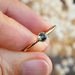Könnte beinhalten: Ein zarter Goldring mit einem kleinen, runden, blaugrünen Edelstein in der Mitte.