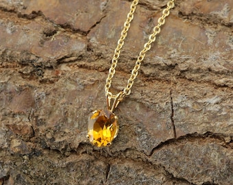 Könnte beinhalten: Eine goldene Kettenkette mit einem runden, ovalen Anhänger aus orangefarbenem Edelstein.