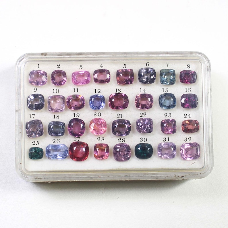 May include: A clear plastic case containing 32 gemstones in various colors, including pink, purple, blue, and green. Each gemstone is a cushion cut and numbered from 1 to 32.
