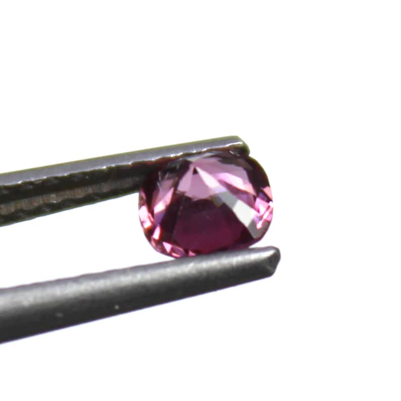 May include: A faceted, round-cut gemstone in shades of pink and purple is held by a pair of tweezers. The gem has multiple facets that reflect light, creating a sparkling effect. The background is plain white.