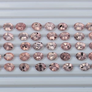Puede incluir: Treinta y seis piedras preciosas rosadas de forma ovalada con inclusiones negras. Las piedras preciosas están dispuestas en seis filas de seis.