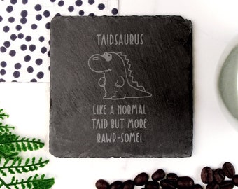 Puede incluir: Un posavasos de pizarra negra con una ilustración de dinosaurio blanca y el texto "Taidsaurus Like a normal taid but more rawr-some!"