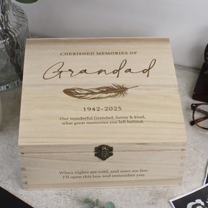 Puede incluir: Una caja de madera con tapa con bisagras y cierre de latón. La caja está grabada con las palabras "Cherished Memories of Grandad 1942-2025" y un diseño de pluma. El texto debajo dice "Nuestro maravilloso Grandad, divertido y amable, qué grandes recuerdos dejaste. Cuando las noches son frías y las estrellas son pocas, abriré esta caja y te recordaré."