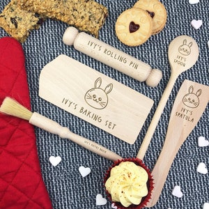 Può includere: Un set da forno in legno con un mattarello, un cucchiaio, una spatola, un pennello da pasticceria e un tagliere. Il set è inciso con il nome "Ivy's Baking Set" e un design a forma di coniglio.