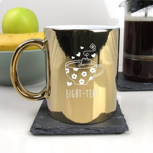 May include: Gold metallic mug with a white design of a teacup with a tea bag and the text "EIGHT-TEA!"