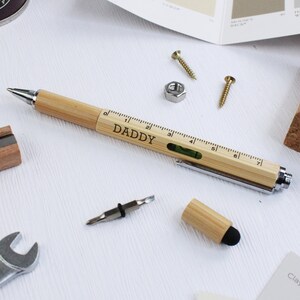 May include: A wooden multi-tool pen with a ruler, spirit level, and screwdriver. The pen is engraved with the word "DADDY".