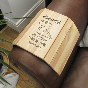 May include: A wooden armrest tray with a dinosaur illustration and the text "Daddysaurus Like a normal daddy but more Rawr-some!"