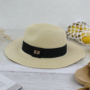 Peut inclure: Un chapeau de paille beige avec un ruban noir et les initiales dor&eacute;es "RB" sur le ruban.