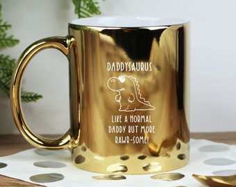 Può includere: Tazza in metallo dorata con un contorno bianco di un dinosauro e il testo "Daddysaurus Like a normal daddy but more rawr-some!"