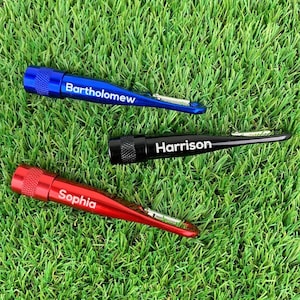 Może przedstawiać: Trzy spersonalizowane latarki z karabińczykiem do kluczy. Latarki są niebieskie, czarne i czerwone. Na latarkach wygrawerowano imiona "Bartholomew", "Harrison" i "Sophia".