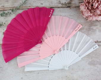 May include: Four hand fans with different colors and text. The top fan is pink with the text "Team Bride". The second fan is pink with the text "Team Bride". The third fan is white with the text "Bride".