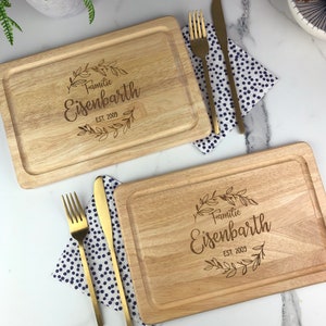 May include: Two wooden cutting boards with a decorative engraved design. The design features a wreath of leaves with the text "Familie Eisenbarth EST. 2009".