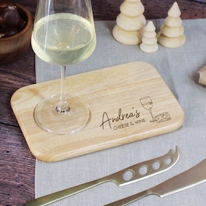 Può includere: Un tagliere in legno personalizzato per formaggio e vino con un porta bicchiere e il testo "Andrea's Cheese & Wine".