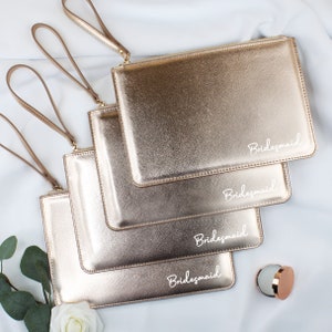 May include: Four gold metallic zippered pouches with the word "Bridemaid" written in white on each pouch.