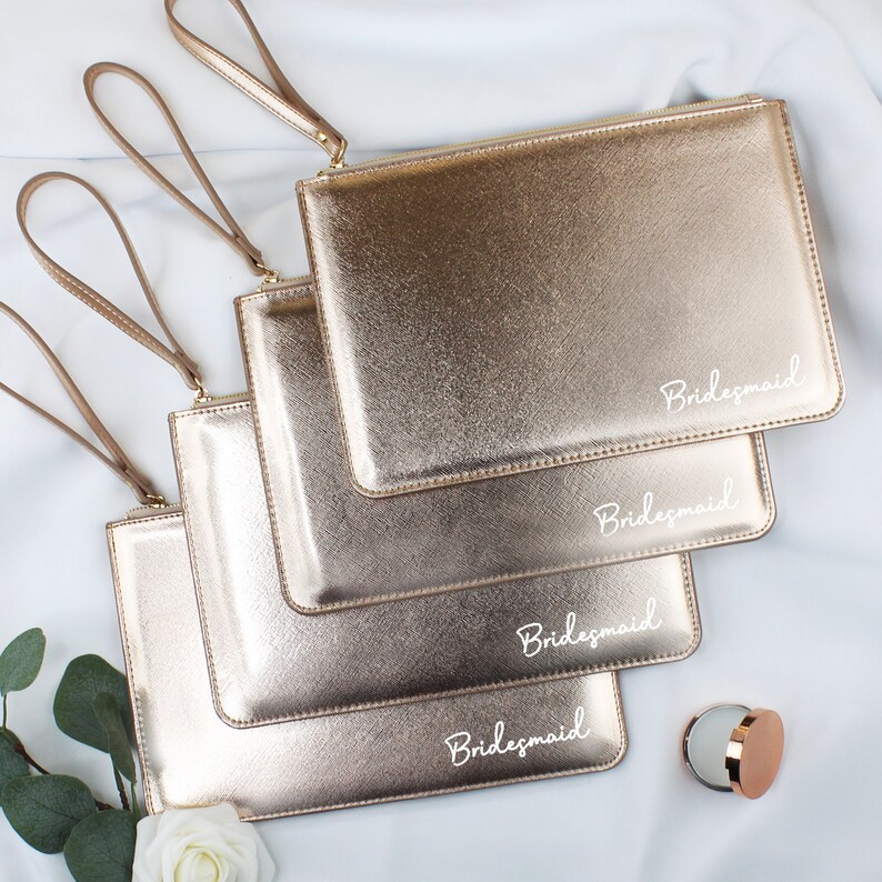 May include: Four gold metallic zippered pouches with the word "Bridemaid" written in white on each pouch.