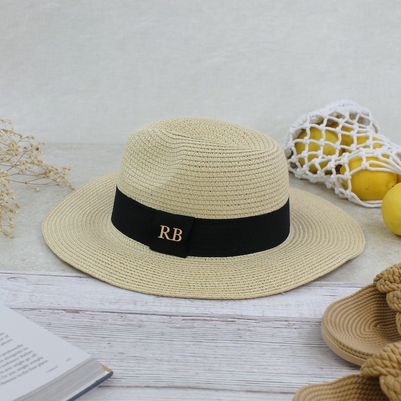 Peut inclure: Un chapeau de paille beige avec un ruban noir et les initiales dor&eacute;es "RB" sur le ruban.
