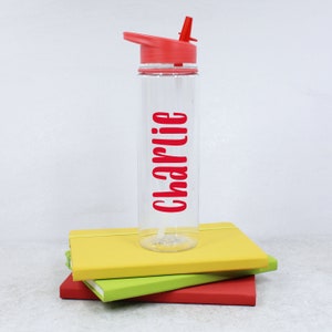 May include: A clear plastic water bottle with a red lid and a straw. The bottle has the name "Charlie" printed on it in red letters.