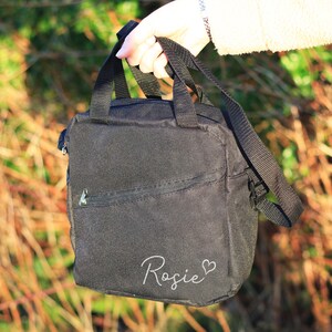 K&ouml;nnte beinhalten: Schwarze Canvas-Tragetasche mit Rei&szlig;verschlussfach und wei&szlig;er Aufschrift "Rosie" mit einem Herzsymbol.
