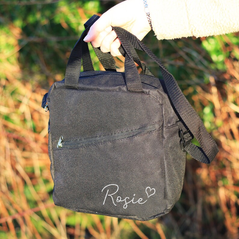 K&ouml;nnte beinhalten: Schwarze Canvas-Tragetasche mit Rei&szlig;verschlussfach und wei&szlig;er Aufschrift "Rosie" mit einem Herzsymbol.
