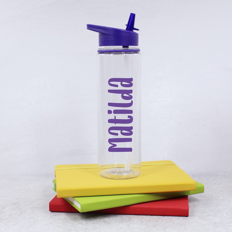 May include: A clear plastic water bottle with a purple lid and straw. The bottle has the name "Matilda" written on it in purple lettering.