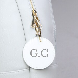May include: A white leather bag with a gold zipper and a white leather keychain with the initials "G.C." embossed on it.