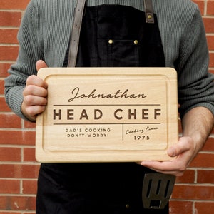 May include: A wooden chopping board with the text "Johnathan Head Chef Dad's Cooking Don't Worry! Cooking Since 1975" engraved on it.