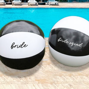 May include: Two black and white beach balls with the words "bride" and "bride squad" written on them.