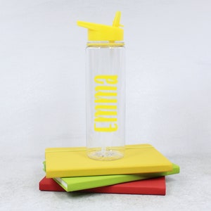 May include: A clear plastic water bottle with a yellow lid and straw. The bottle has the name "Emma" printed on it in yellow.