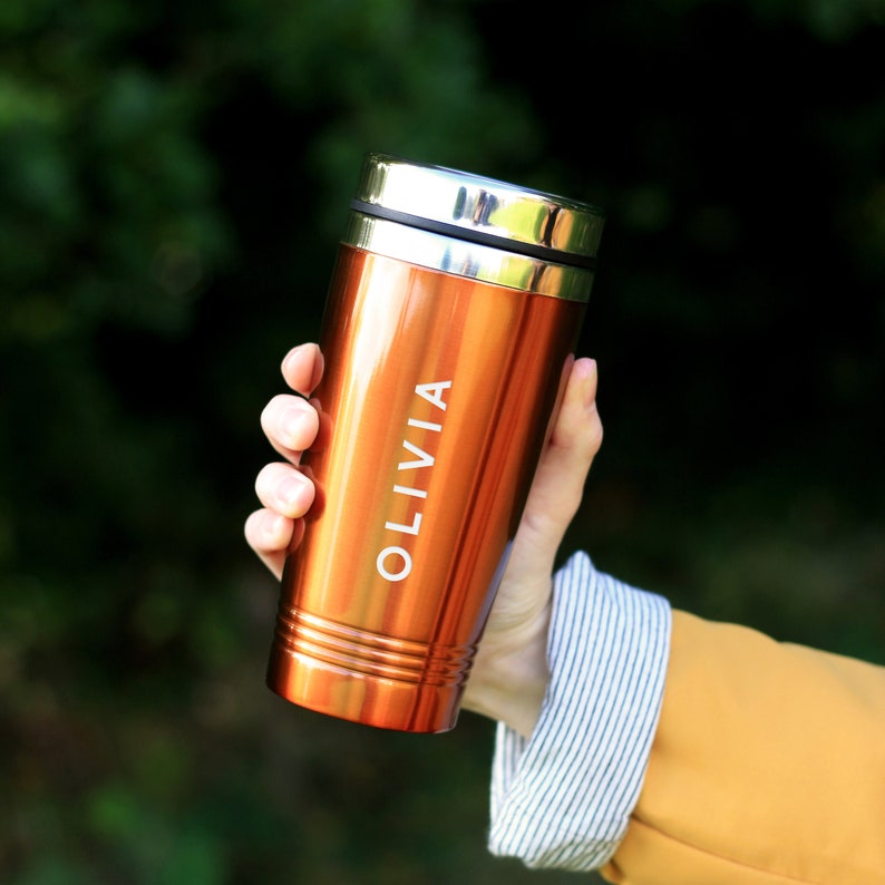 May include: A copper-colored travel mug with a silver lid and the name "Olivia" engraved on the side.