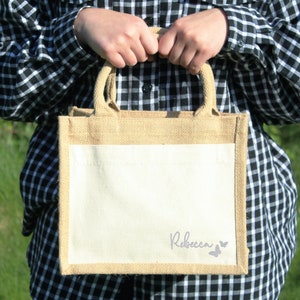 May include: A natural jute tote bag with a white cotton panel. The bag has a personalised name, "Rebecca", and two purple butterfly silhouettes.