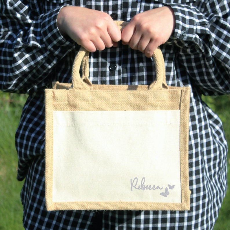 May include: A natural jute tote bag with a white cotton panel. The bag has a personalised name, "Rebecca", and two purple butterfly silhouettes.