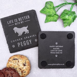May include: Two black slate coasters. One coaster has the text "LIFE IS BETTER WITH MY COCKER SPANIEL PEGGY" with a dog silhouette and paw prints. The other coaster has the text "HAPPY BIRTHDAY RACHEL LOTS OF LOVE FROM MUM XX".