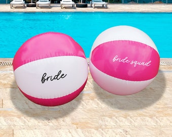 May include: Two pink and white beach balls with the words "bride" and "bride squad" written on them.